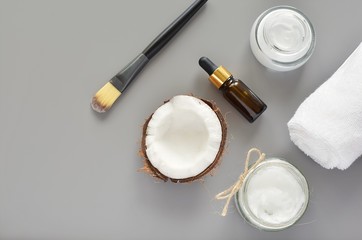 Modern composition with coconut oil cosmetic products for hair oi skin, body lotion, essential oil, cosmetic brush, towel, coconut shell, gray background