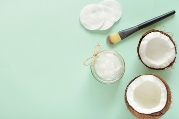 Coconut oil for skin or hair cosmetic, flat lay on green background with coconut shells, cosmetic brush, copy space