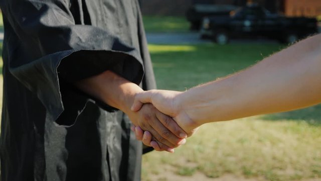 Successful Asian man in graduate clothes accepts congratulations. They shake his hand