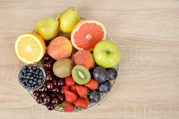 Acceptable fruits for diabetes. In a plate are orange, grapefruit, cherry, plum, pears, peaches, apple, plum, blueberries, kiwi. View from above. Light background. Free space for text.