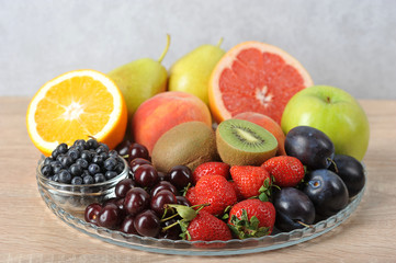 Acceptable fruits for diabetes. In a plate are orange, grapefruit, cherry, plum, pears, peaches, apple, plum, blueberries, kiwi. Light background. Close-up.