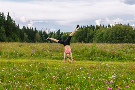 Young Woman Doing Exercises Cartwheel In A Meadow Outside The City