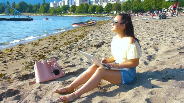 A young freelancer works on her laptop at the beach.