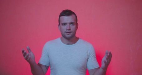 Handsome man in white t-shirt staying from of camera and acting emotions of shocked , happiness , surprised face, clap and smiling on red and rose background , slow motion shot. 