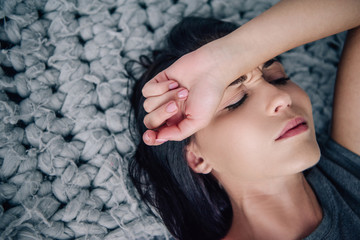 beautiful depressed woman lying on bed with hand on forehead at home