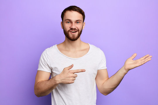 young man reccomend the goods. happy awesome bearded man pointing away. close up portrait. isolated blue background. copy space
