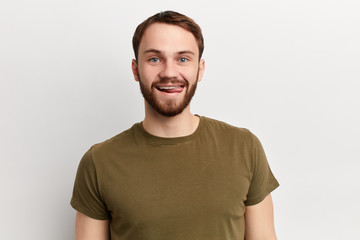 handsome playful young man wears green t shirt ,shows tongue isolated over white background. close up photo. emotion, facial expression