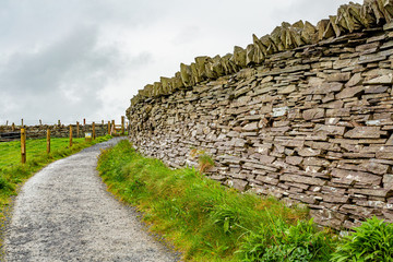 Fototapeta na wymiar Natural limestone wall next to a path with fence of wooden poles and wire in the Burren, geosites and geopark, spring day in the countryside in County Clare in Ireland