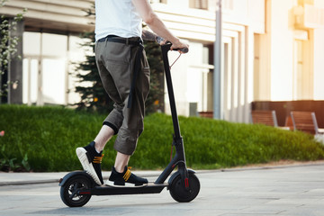 Close up of man riding black electric kick scooter at beautiful park landscape