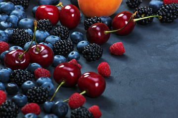 Blackberries,blueberries,raspberries,cherries,apricot on black concrete background. Healthy food