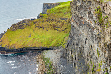 View of a side wall of a cliff and hills with green grass along the coastal walk route from Doolin to the Cliffs of Moher, geosites and geopark, Wild Atlantic Way, county Clare in Ireland