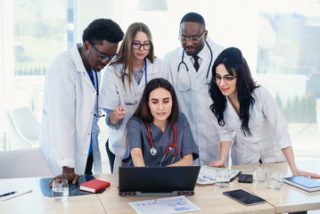 Group of multi national doctors using laptop for discussing analysis in the conference room. Side...