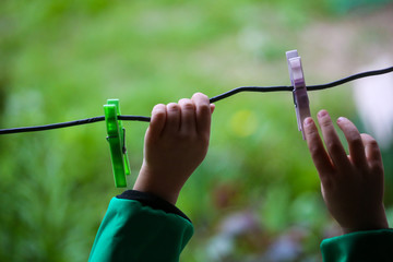 Details with the hands of a little girl playing with plastic clothes pegs on a wire