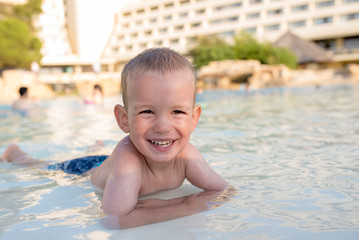 Fototapeta na wymiar Adorable smiling boy looking at camera while having fun in outdoor swimming pool
