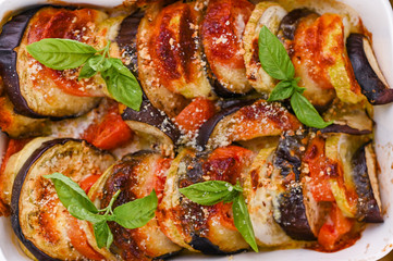 Traditional italian food. Eggplant and tomatoes with parmesan. Baked summer wax with sauce, cheese and basil. Healthy lunch for the family.