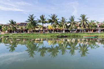 Fototapeta na wymiar Hoi An, Vietnam - June 2019: reflection of palm trees, houses and boats in the river water