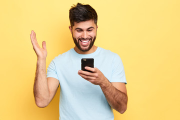 cheerful positive overjoyed man holds smart phone, reads something funny, raises palm,People and...