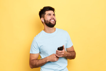 Excited cheerful man using smartphone, looking up, enjoying listening to music, isolated yellow background, studio shot. hobby, lifestyle, free time, spare time