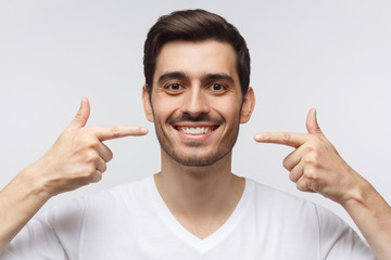 Portrait of smiling young man pointing to his perfect natural white teeth after whitening...