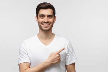Handsome young man in white t-shirt pointing right with his finger, isolated on gray background
