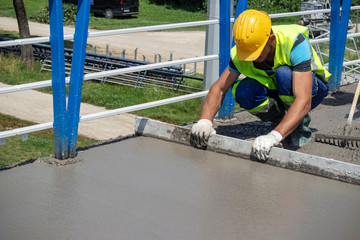 Worker with yellow helmet straighten and smoothing fresh concrete on a construction site
