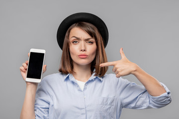 Brunette girl in hat and shirt showing you notification in smartphone