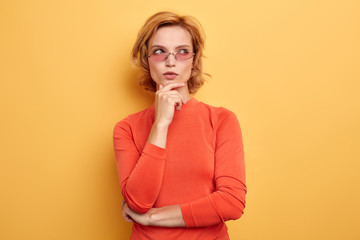 Beautiful young girl htful with hand on chin thinking about question, pensive expression.girl trying to solve a problem. isolated yellow background