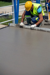 Worker with yellow helmet straighten and smoothing fresh concrete on a construction site