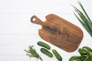 top view of wooden cutting board, cucumbers and greenery