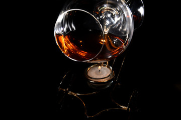 Fototapeta na wymiar A glass of cognac on a special stand with candle for warming drink in the dark