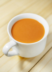 Hot milk tea in a white cup on wooden