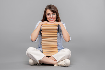 Young smiling female student with her chin over high stack of books