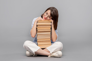 Clever female stuudent with crossed legs keeping her head on top of books