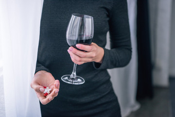 Cropped view of depressed woman with wine glass and pills at home
