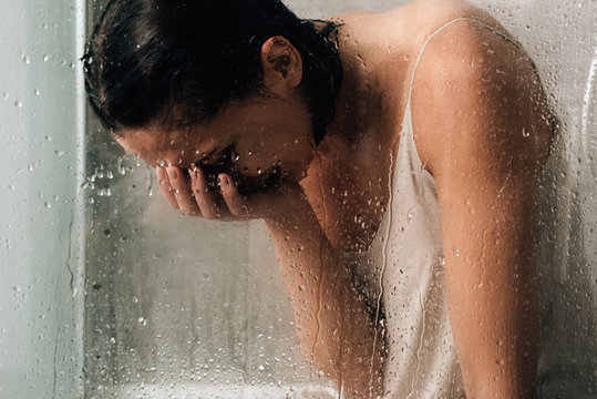 lonely depressed woman crying in shower through glass with water drops