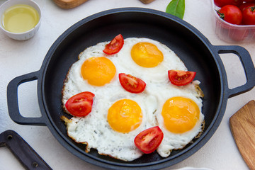 Frying pan with fried eggs, tomatoes on a white background