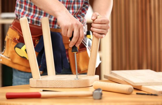 Young working man repairing wooden stool using screwdriver indoors, closeup
