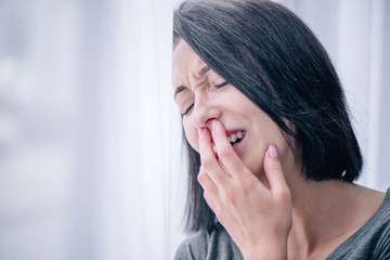 selective focus of depressed brunette woman covering mouth and crying at home