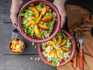 Female hands hold a plate with vegan salad with fried peach. Top view