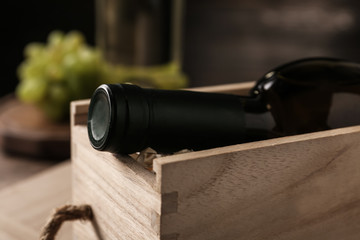 Open wooden crate with bottle of wine on blurred background