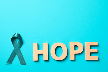 Word Hope made of wooden letters and teal awareness ribbon on light blue background. Symbol of social and medical issues