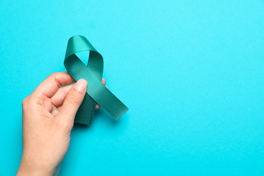 Woman holding teal awareness ribbon on light blue background, top view with space for text. Symbol of social and medical issues