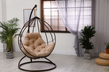Comfortable swing chair with pillow in room interior