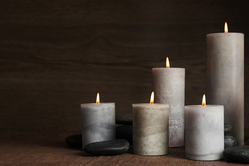 Fototapeta na wymiar Burning candles and spa stones on wooden table, space for text