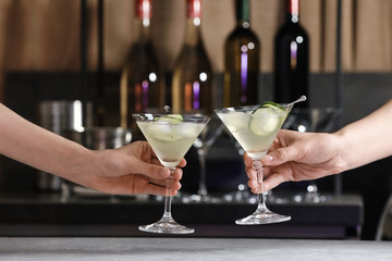 Young people clinking glasses of tasty cucumber martini at bar counter, closeup