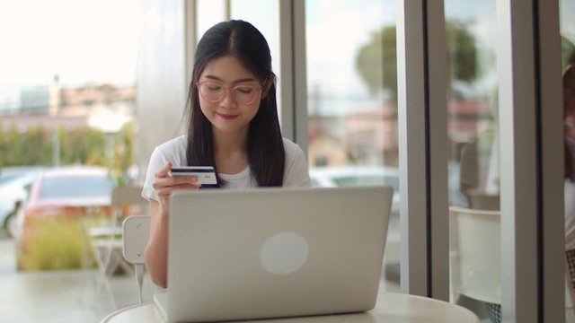 Freelance Asian women online shopping at coffee shop. Young Asia Girl using laptop, credit card buy and purchase e-commerce on internet on table at an outdoor cafe in evening concept. Slow motion
