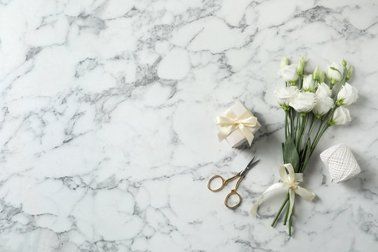Flat lay composition with scissors and flowers on white marble background, space for text