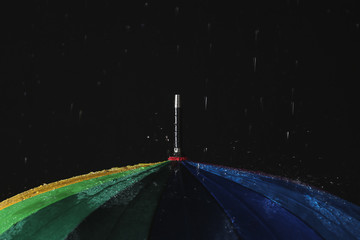 Opened color umbrella under rain against black background, closeup