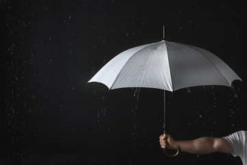 Man holding opened white umbrella under rain against black background, closeup