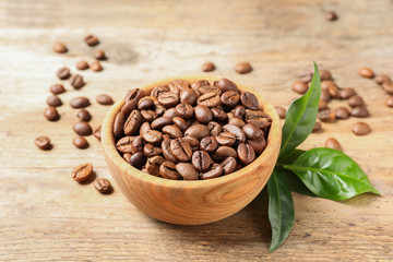 Bowl of coffee beans and fresh green leaves on wooden table